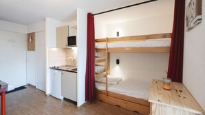 A compact room with a bunk bed, kitchenette, and a small table with a candle. - Nice 4pers apartment. mountain style in a quiet residence with ski-to-door departure (VAL THORENS)