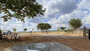 A picnic area with a metal ring, picnic table, and trees in a rural setting. - Campsite near Wichita Wildlife Refuge & Mountains (Cache)