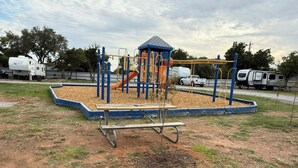 A playground with a slide and climbing structures, surrounded by a fenced area with picnic tables. - Campsite near Wichita Wildlife Refuge & Mountains (Cache)
