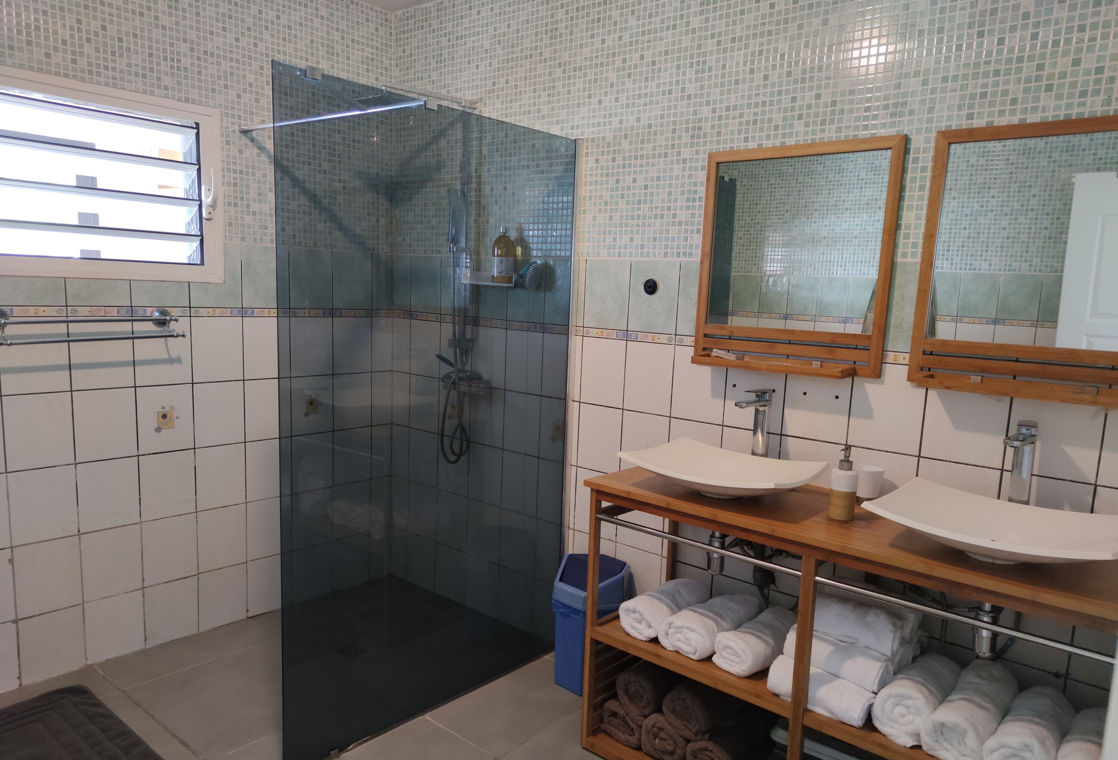 A bathroom with a glass-enclosed shower, two sinks, and a shelf with towels.