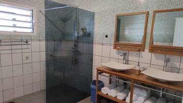 A bathroom with a glass-enclosed shower, two sinks, and a shelf with towels.