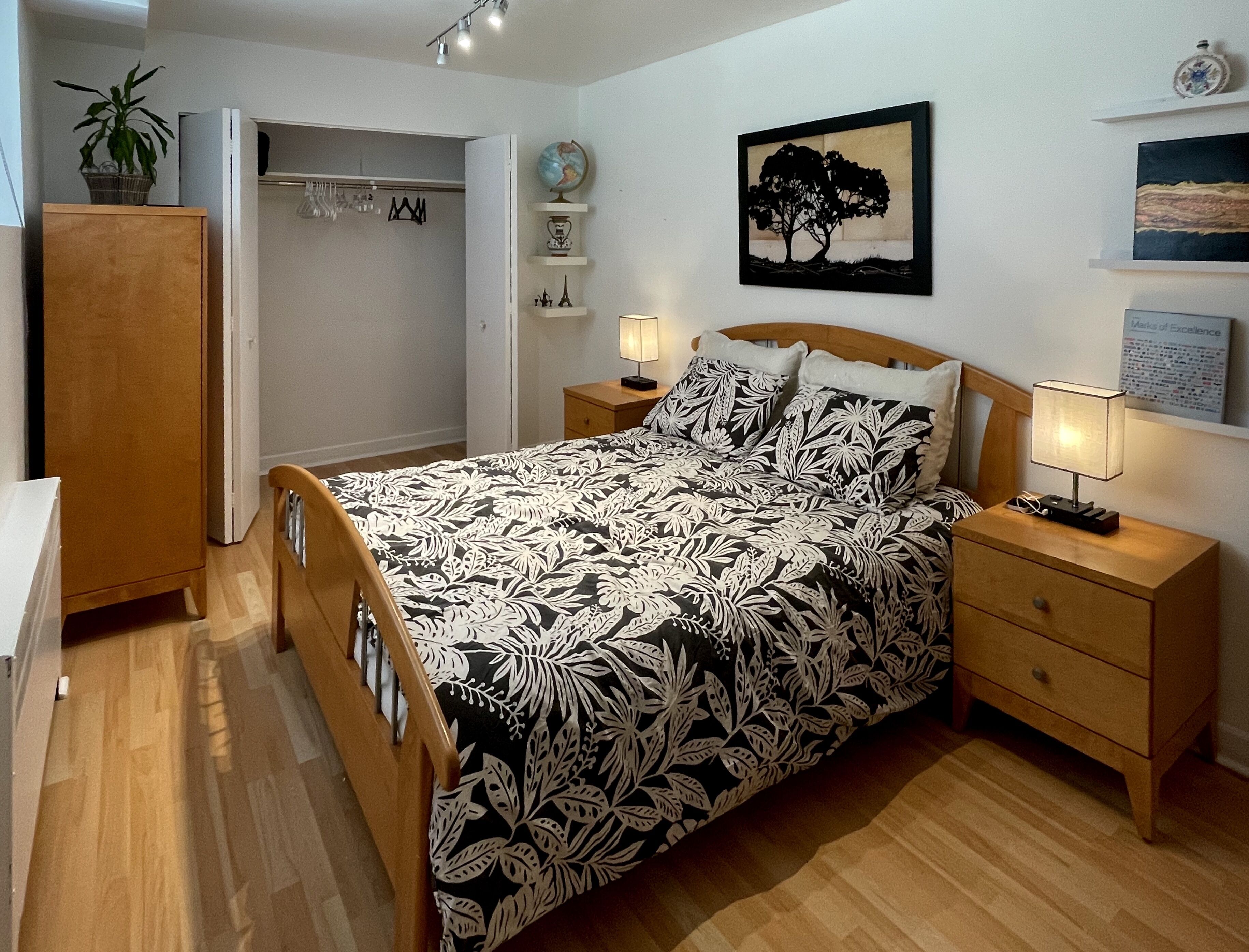 A bedroom with a bed, wooden nightstands, a dresser, a wardrobe, a globe, a framed picture of a tree, and a lamp.