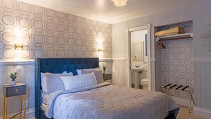 A bedroom with a large bed, a nightstand, a dresser, a vanity with a mirror, and a hanging towel rack. - Boho Manor Resort - Room C (Monte Rio)