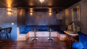 A modern lounge area with a blue cushioned bench, two round tables, and a chandelier. - Boho Manor Resort - Room C (Monte Rio)