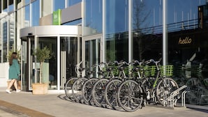 Un edificio moderno con fachada de vidrio, un letrero verde que dice "ibis styles" y una fila de bicicletas estacionadas afuera.