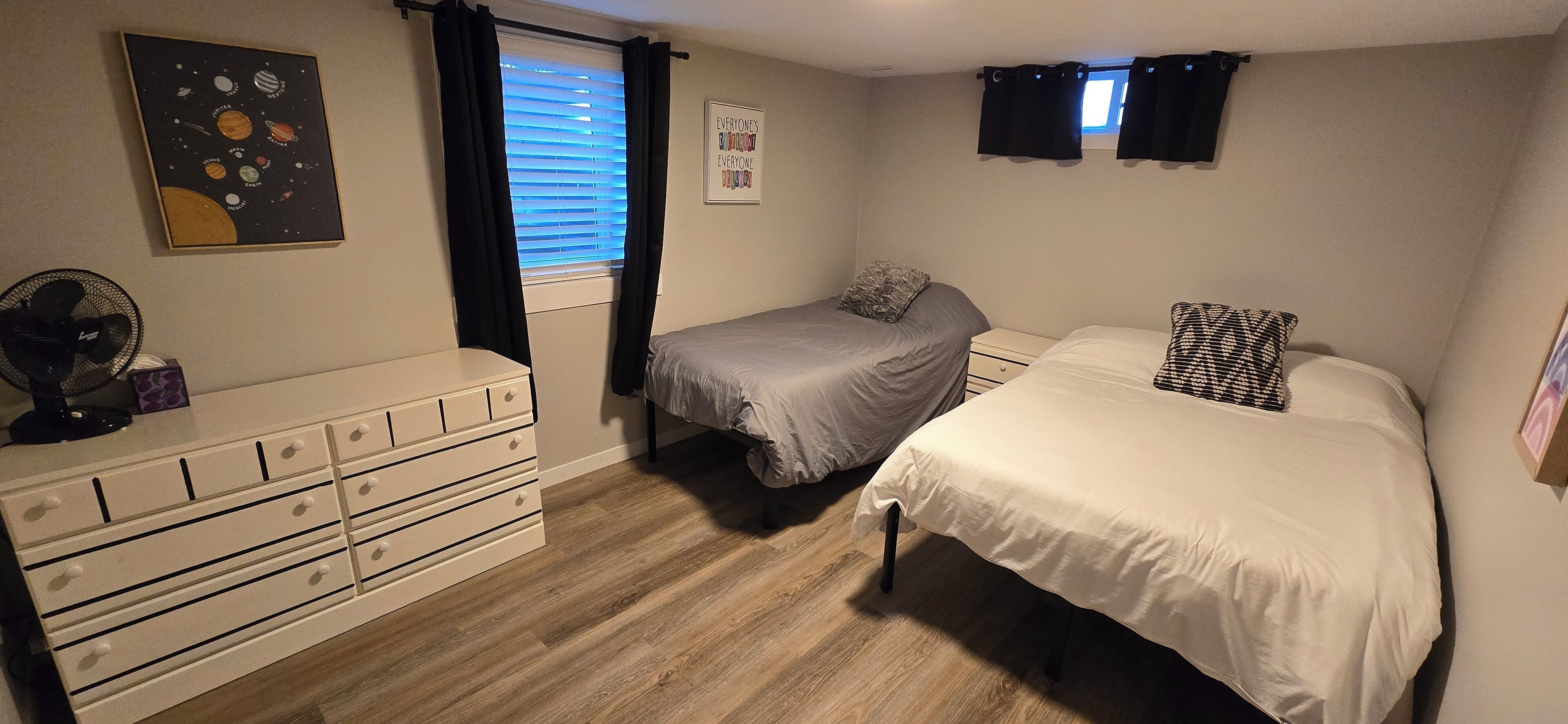 A bedroom with two beds, a dresser, a ceiling fan, and a window with blinds.