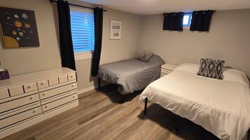 A bedroom with two beds, a dresser, a ceiling fan, and a window with blinds.