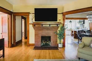 Una sala de estar con chimenea de ladrillo, un televisor de pantalla plana montado arriba y un comedor al fondo.