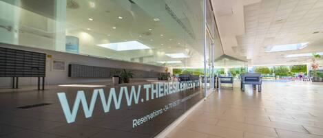 A modern hotel lobby with a glass facade, a reception desk, and a seating area.