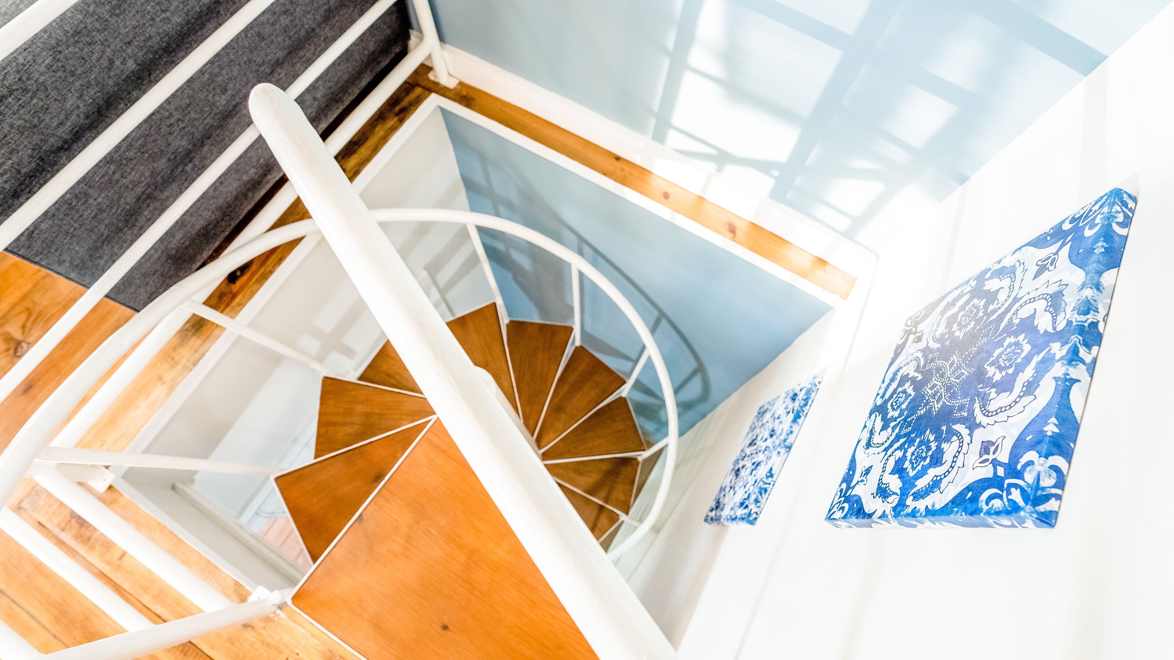 A spiral staircase with wooden steps and white railings, leading to a room with a blue patterned wall.