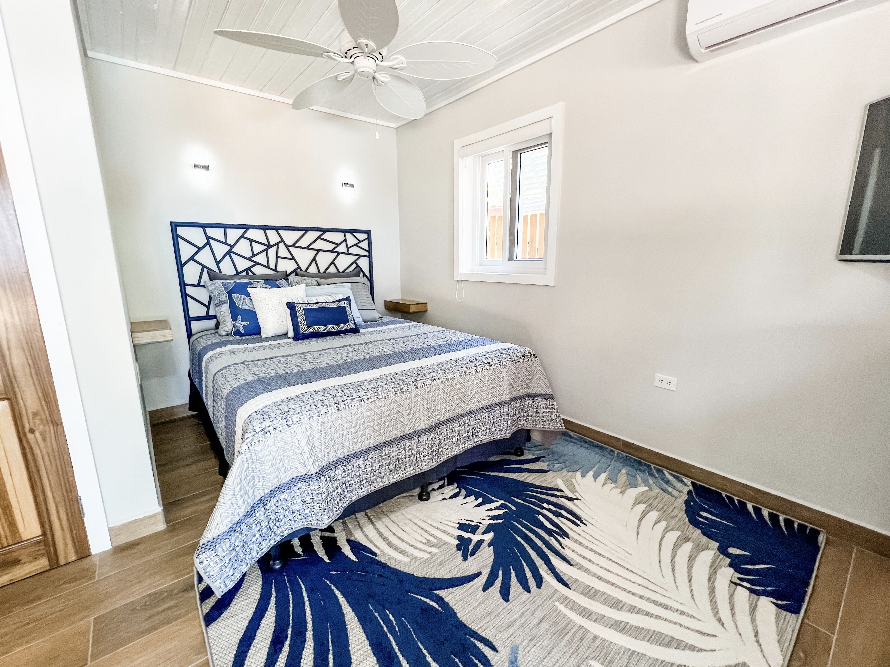 Ein Schlafzimmer mit Bett, Deckenventilator, Fenster und Wandklimaanlage.