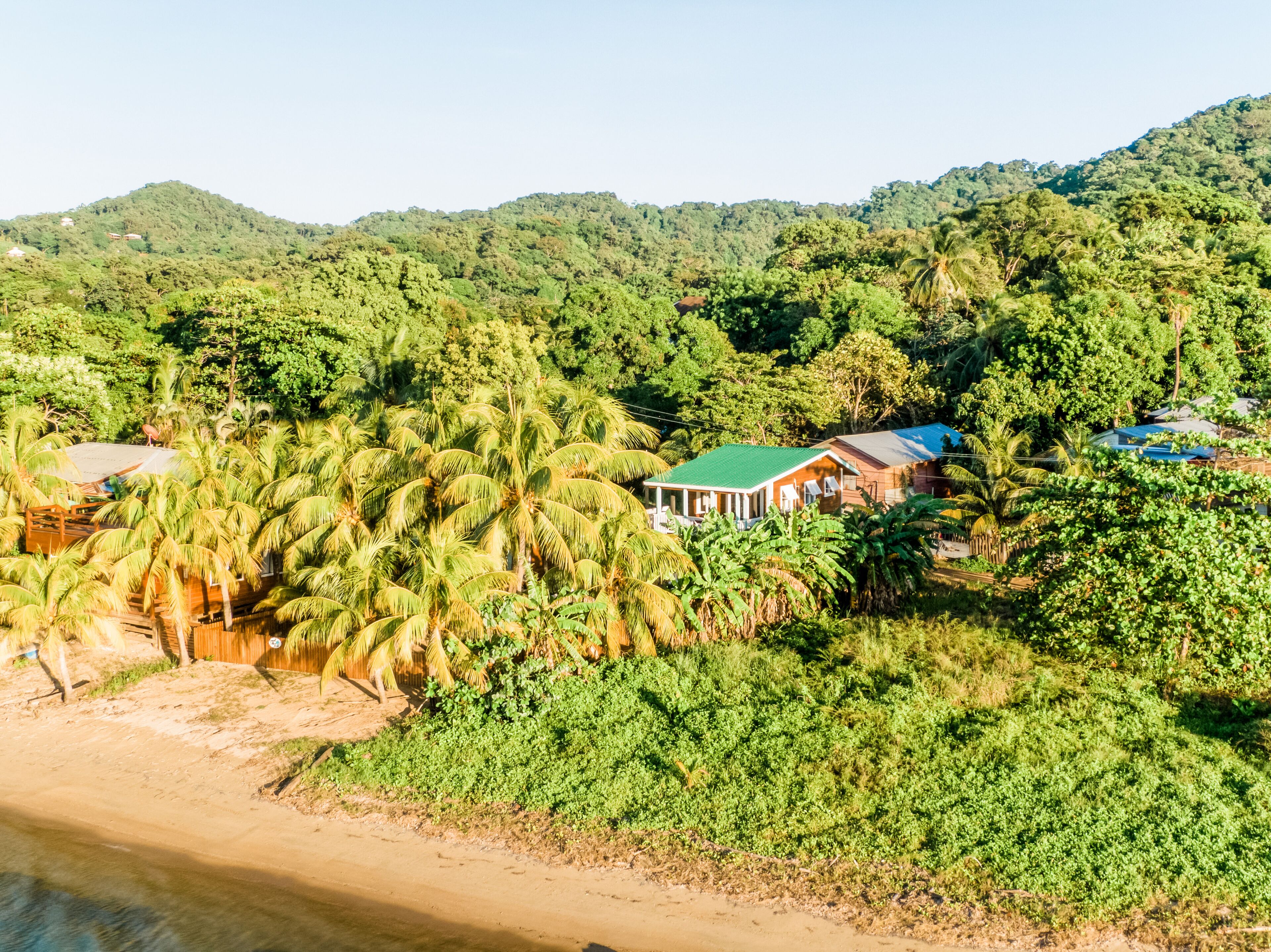 Una zona costiera con case immerse in una fitta vegetazione tropicale e colline sullo sfondo.
