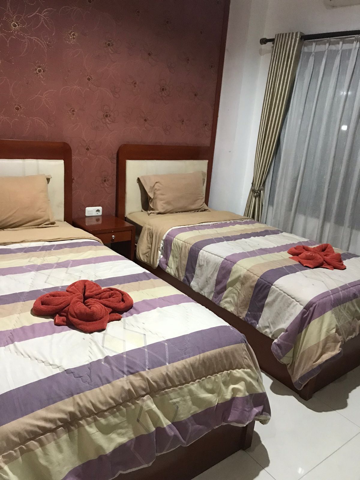 A hotel room with two beds, each with a striped bedspread and a red towel.