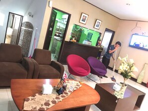 A hotel lobby with brown sofas, a wooden coffee table, a reception desk, and a TV screen. - Rizh Hotel (Bandung)