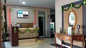 A reception area with a counter, a television mounted on the wall, and a decorative mirror. - Rizh Hotel (Bandung)