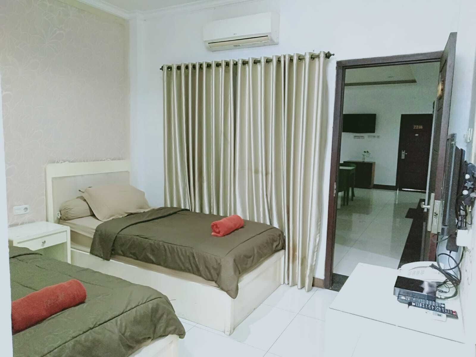 A hotel room with two beds, a desk, an air conditioner, and a sliding door to a balcony.