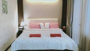A neatly made bed with a white and pink bedding, a bedside lamp, and a telephone on the nightstand. - Rizh Hotel (Bandung)