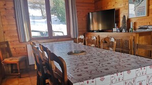 Une cabane en bois avec une table à manger, des chaises, un téléviseur et une fenêtre donnant sur un paysage enneigé.