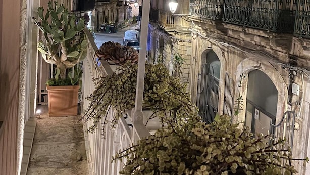 A narrow street with buildings on either side, a street lamp, and a potted plant.