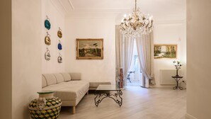 A living room with a sofa, a coffee table, a chandelier, and two paintings on the wall. - Palazzo Dello Spagnolo Suite (Naples)