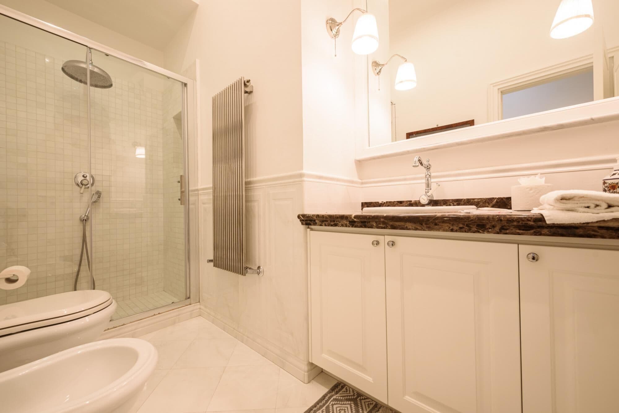 A bathroom with a glass-enclosed shower, a toilet, a sink with a marble countertop, and a mirror above the sink.