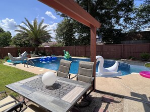 Relax by the pool surrounded by a tranquil backyard with a pergola, dining area, and plenty of space to play.