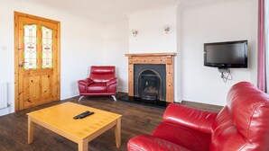 A living room with a wooden coffee table, red leather sofa, a fireplace, and a television mounted on the wall. - An Rua (500m to Lahinch Beach), An Rua - 15 min walk to Lahinch Golf Club (Lahinch Road)