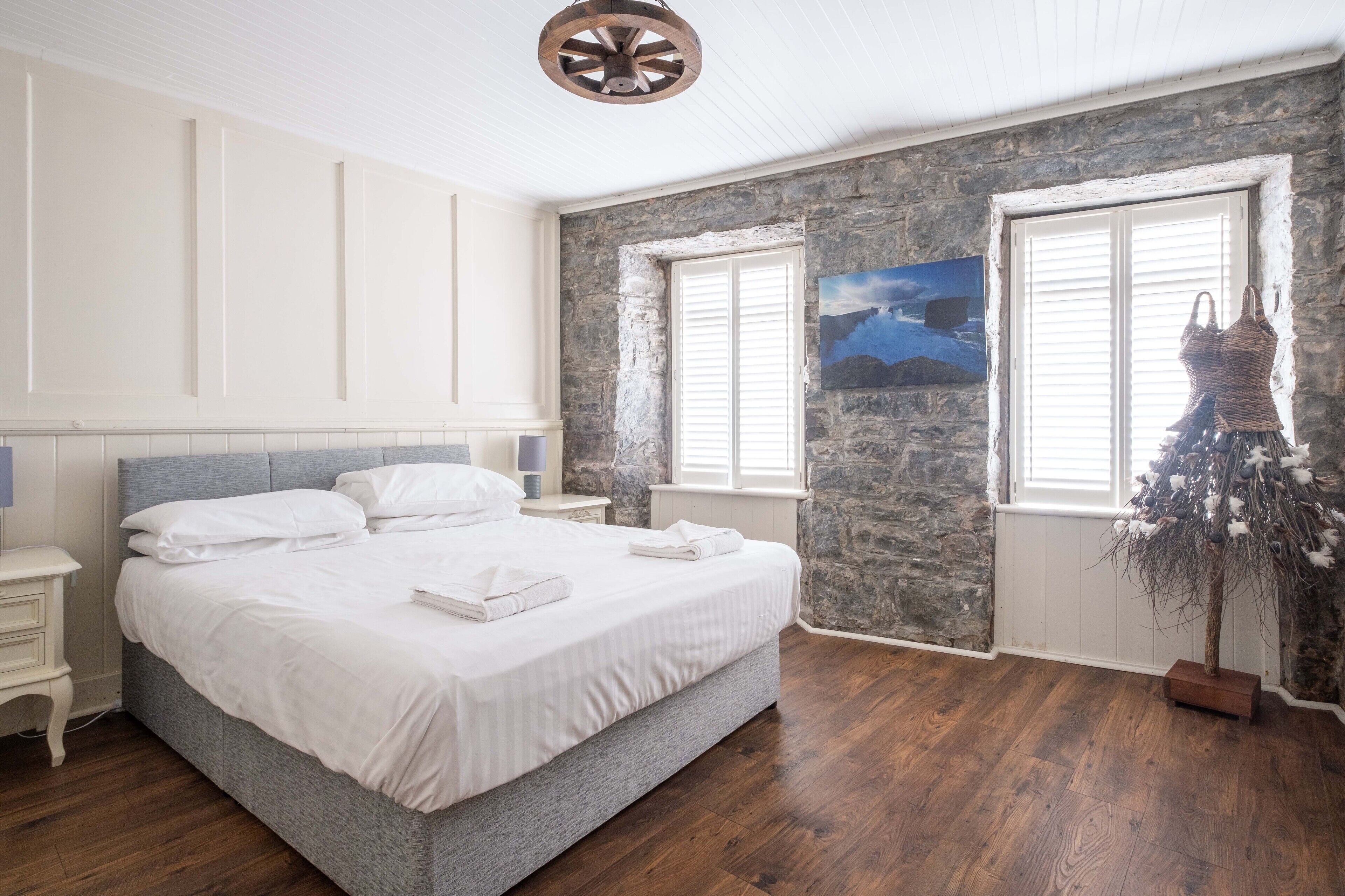 Een slaapkamer met een groot bed, witte beddengoed, een stenen muur en een raam met uitzicht op de bergen.