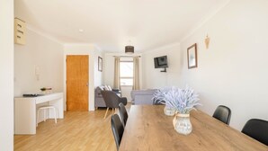 A spacious living area with a wooden dining table, a sofa, and a TV mounted on the wall. - Dough Beag 10 (250m to Lahinch Beach), Dough Beag Apartment (Lahinch)