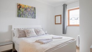 A bedroom with a bed, a nightstand, a window with curtains, and a painting on the wall. - Dough Beag 10 (250m to Lahinch Beach), Dough Beag Apartment (Lahinch)