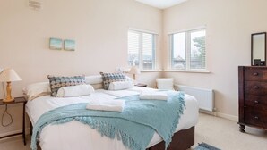 Une chambre à coucher avec un grand lit, deux tables de chevet, une commode et une fenêtre avec des stores.