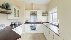 Une cuisine avec des meubles blancs, une cuisinière, un évier et une fenêtre.
