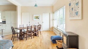 Un vaste espace de vie comprenant une table et des chaises en bois pour la salle à manger, une cheminée et une grande fenêtre équipée de stores.