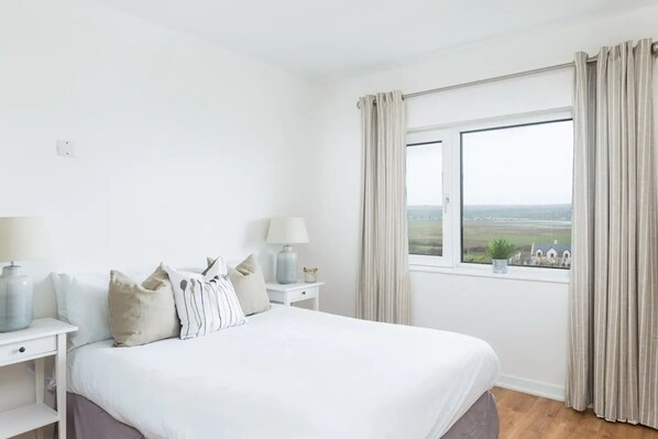 A bedroom with a large bed, two bedside tables, and a window with curtains.