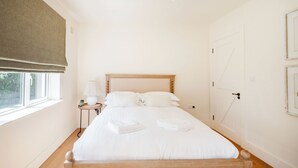 A neatly made bed with white linens and towels, a bedside table with a lamp, and a window with a blind. - The Links 10, Amazing Location- Food, Drinks, Surf, & Golf! - 10 (Lahinch)