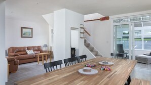 Ein großzügiger Wohnbereich mit einem Holzesstisch, einem braunen Ledersofa und einer Treppe, die in ein Obergeschoss führt.
