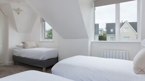 Ein Schlafzimmer mit zwei Betten, einer geneigten Decke und einem Fenster mit Blick auf eine Wohngegend.