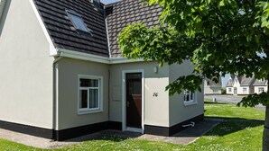 A single-story house with a dark roof, a white door, and a number '76' on the wall. - The Links 16, Amazing Location- Food, Drinks, Surf, & Golf 16 (Lahinch)