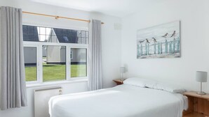 A bedroom with a large bed, a window with curtains, a radiator, and a painting of birds on a fence. - The Links 16, Amazing Location- Food, Drinks, Surf, & Golf 16 (Lahinch)