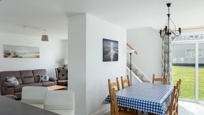 A modern living room with a sofa, a dining table with chairs, a staircase, and a view of the outdoors. - The Links 16, Amazing Location- Food, Drinks, Surf, & Golf 16 (Lahinch)