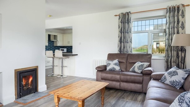 A living room with a fireplace, a sofa, a coffee table, and a view of the outdoors through a window. - The Links 16, Amazing Location- Food, Drinks, Surf, & Golf 16 (Lahinch)