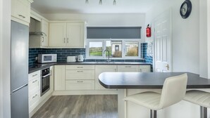 A modern kitchen with white cabinets, a black countertop, a microwave, a kettle, and a view of the outdoors through a window. - The Links 16, Amazing Location- Food, Drinks, Surf, & Golf 16 (Lahinch)
