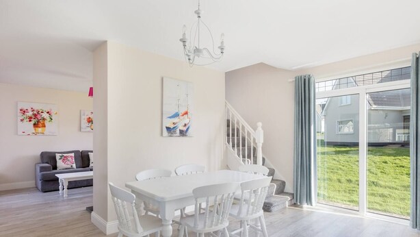 Ein geräumiges Wohnzimmer mit einem weißen Esstisch und Stühlen, einem grauen Sofa und einer Treppe, die zu einem Balkon führt.