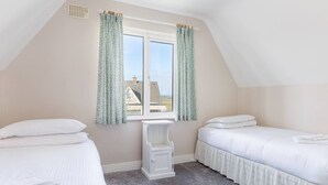 Ein Schlafzimmer mit zwei Betten, einem Vorhangfenster, einer weißen Bank und Blick auf Häuser.