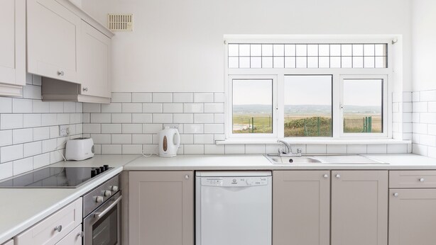 Una cocina moderna con armarios blancos, horno empotrado, lavavajillas y ventana con vistas al campo.