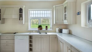 Eine moderne Küche mit weißen Schränken, einem eingebauten Geschirrspüler, einem Fenster mit Gartenblick und einer Arbeitsplatte mit Toaster und Wasserkocher.