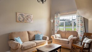 Ein Wohnzimmer mit zwei Sofas, einem Holztisch, einem Schaukelstuhl, einem Wandbild mit einer Globus-Darstellung und einem Fenster mit Vorhängen.