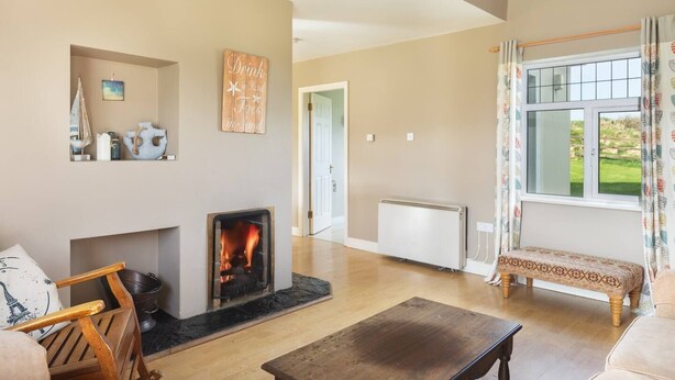 Ein geräumiges Wohnzimmer mit Kamin, einer Bank und Blick auf einen Garten durch ein großes Fenster.