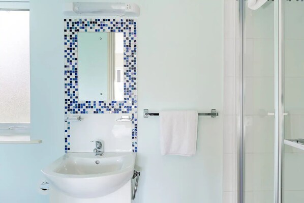Une salle de bain avec un lavabo blanc, un pare-feu en carrelage, un miroir et une douche en verre.
