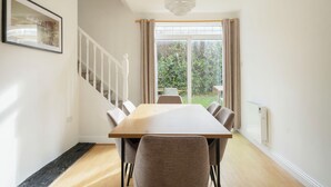 A dining area with a long table, chairs, a staircase, and a view of greenery outside. - The Links 08, Amazing Location- Food, Drinks, Surf, & Golf! - 8 (Lahinch)